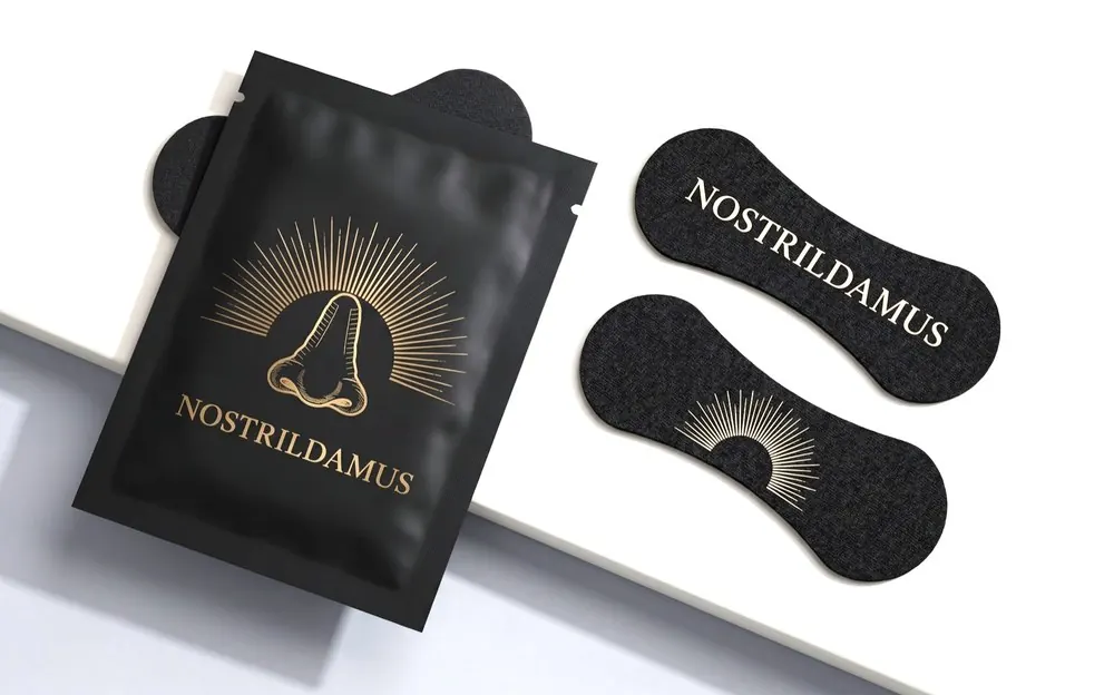 Black Nostrildamus nasal strips stamped in gold beside their foil sachet